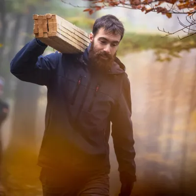 Teilnehmer trägt Holzpfosten auf der Schulter