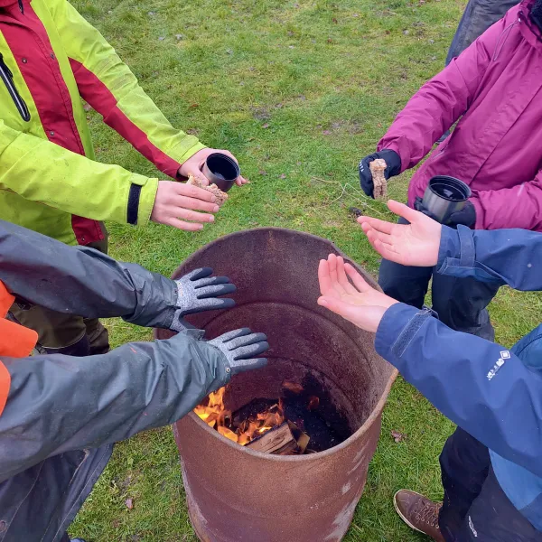 Acht Handpaare wärmen sich am Feuer über einer Tonnen